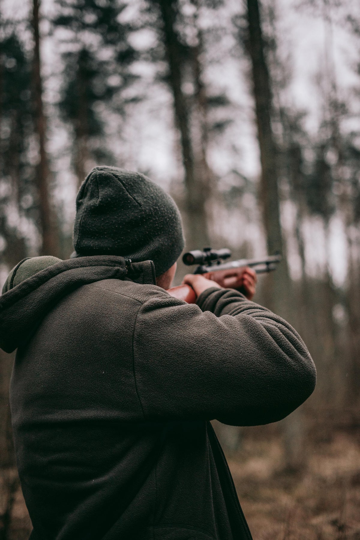 Shooter in a hooded jacket aiming a handgun in the woods
